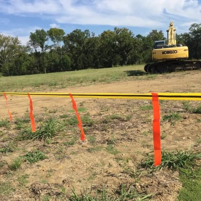 Yellow and orange barricade tapes being used to close off an area. A large yellow excavator is in the background.